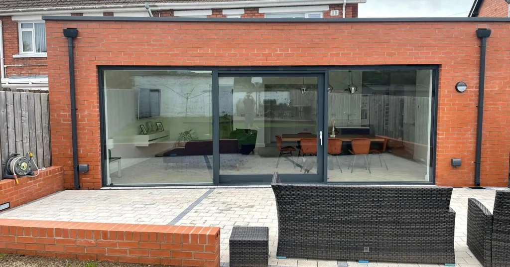 Red brick rear extension with wide dark glazing and a paved terrace