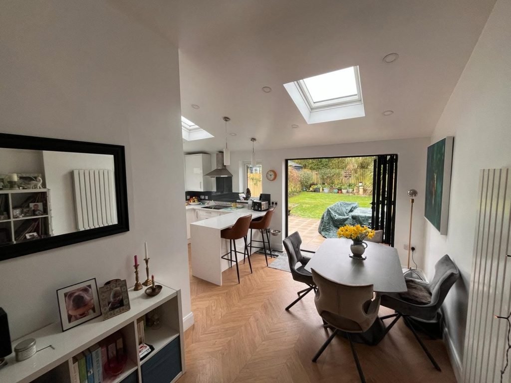 White kitchen and dining table with rooflights and bifold doors open to the garden