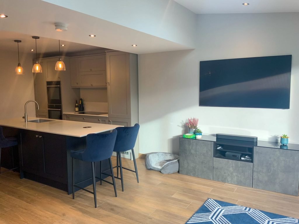 Navy kitchen island with blue stools beside a fitted media unit and television