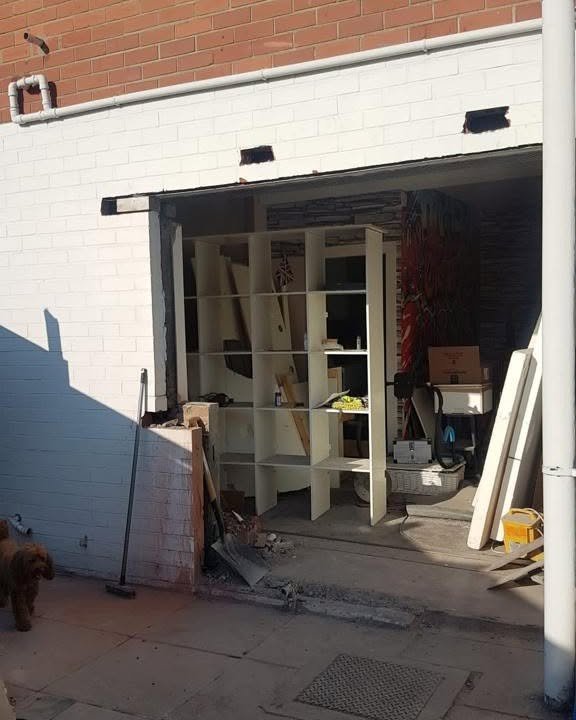 Open garage entrance with shelving and stored items before conversion