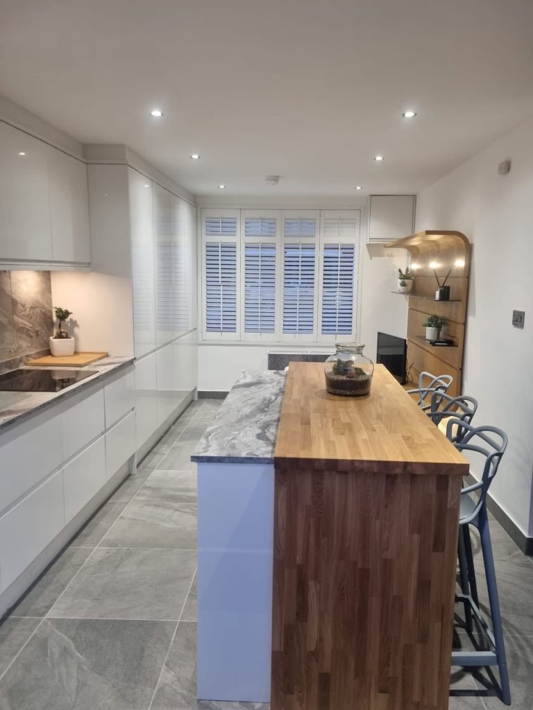 Light grey kitchen with a timber breakfast bar, tiled floor and window shutters