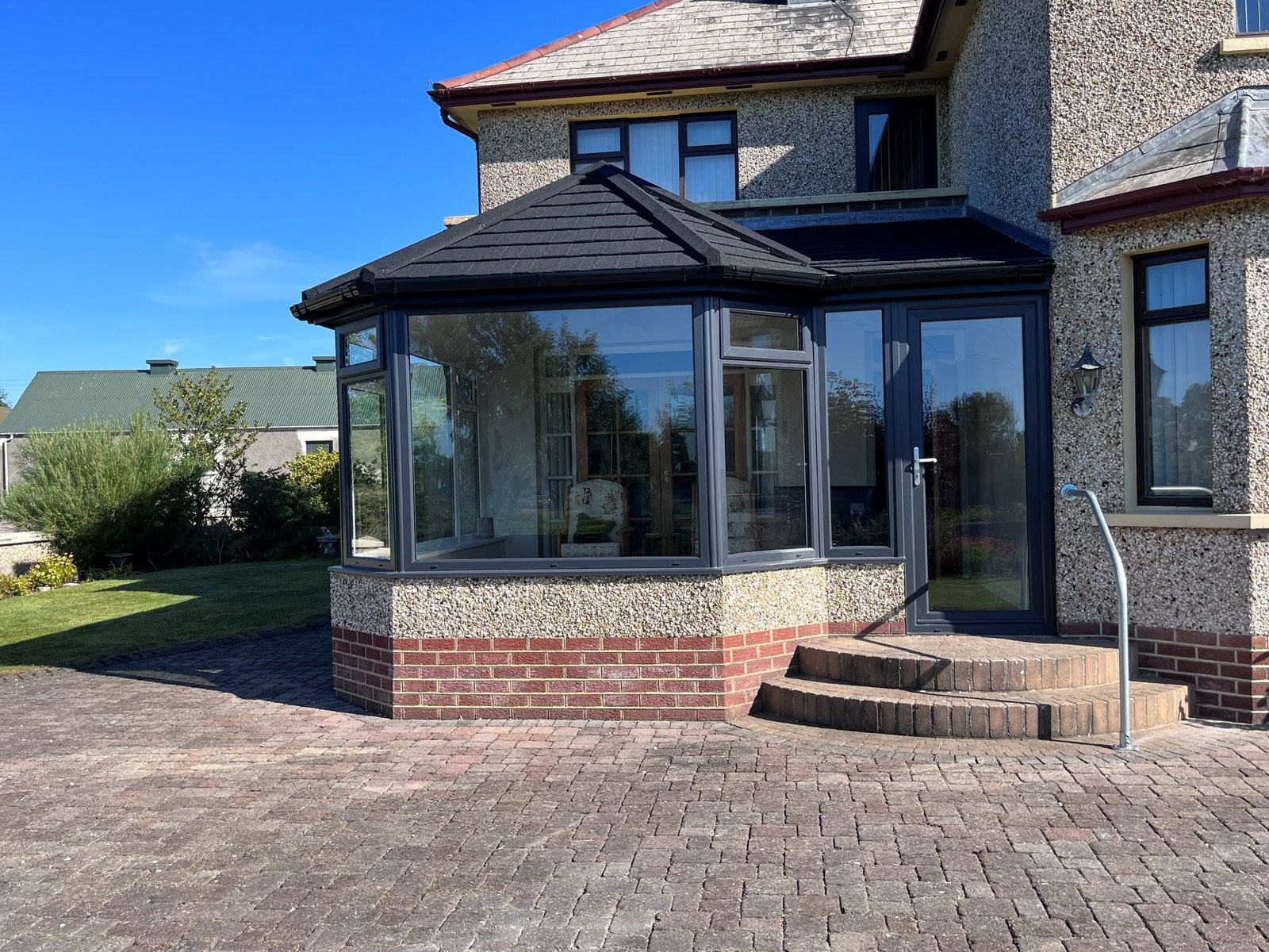 Anthracite conservatory with a dark tiled roof, brick plinth and steps to the house