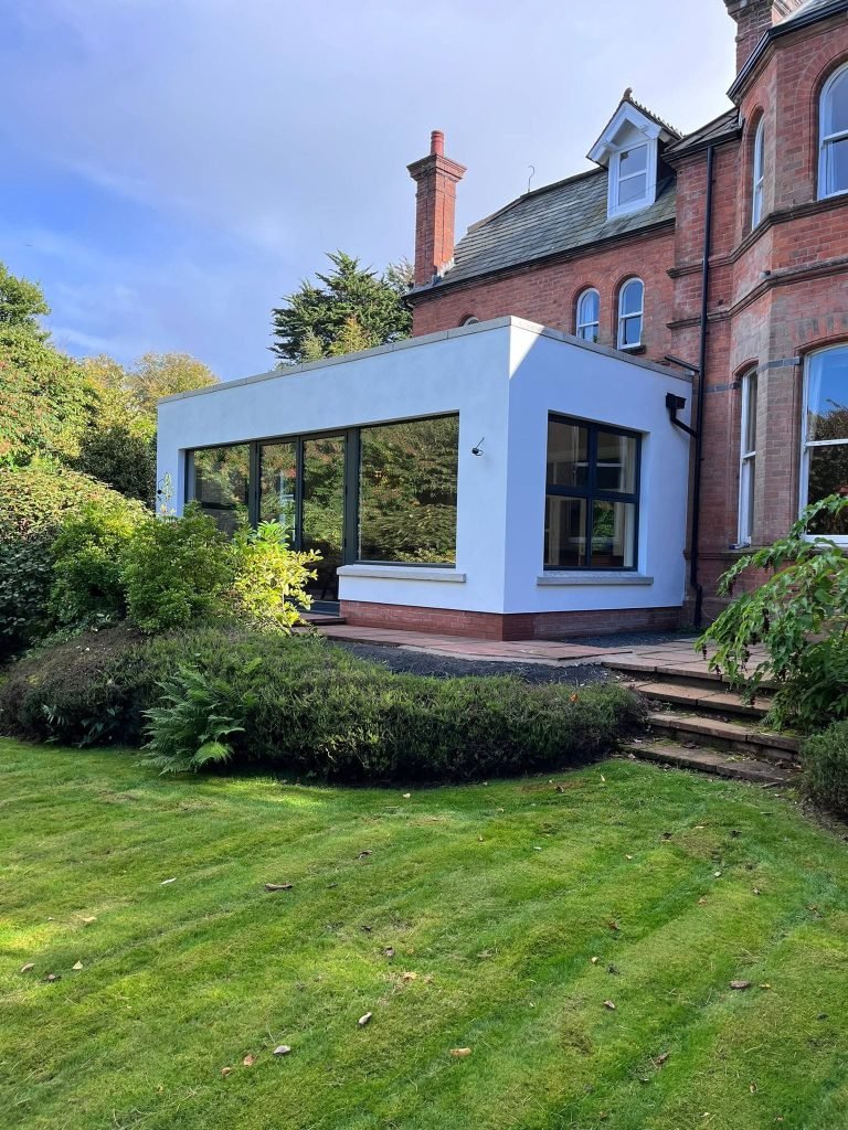 White rendered extension with dark garden glazing beside the original red brick house