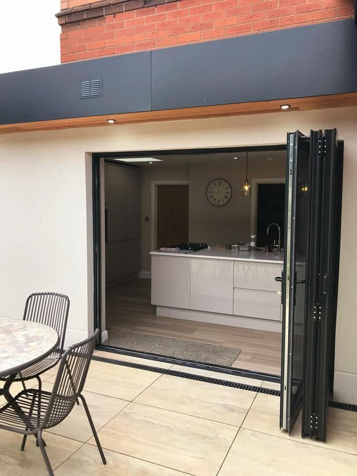 Three leaf anthracite bifold doors folded open between the cream rendered extension and patio