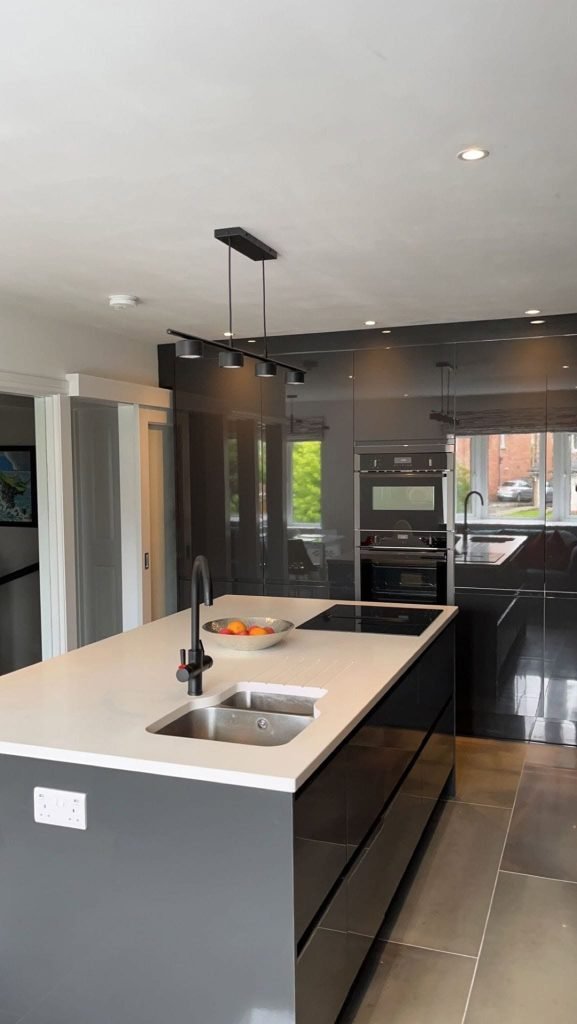 Grey glossy kitchen island with a sink and hob beside a glazed partition