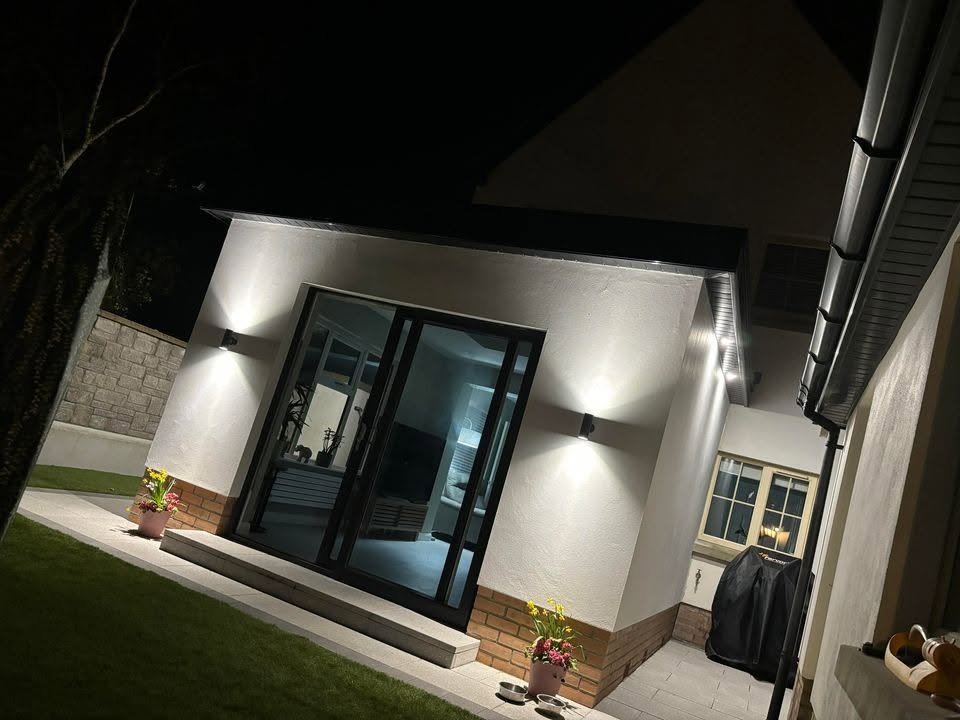 White rendered extension with dark garden doors and exterior lights at night