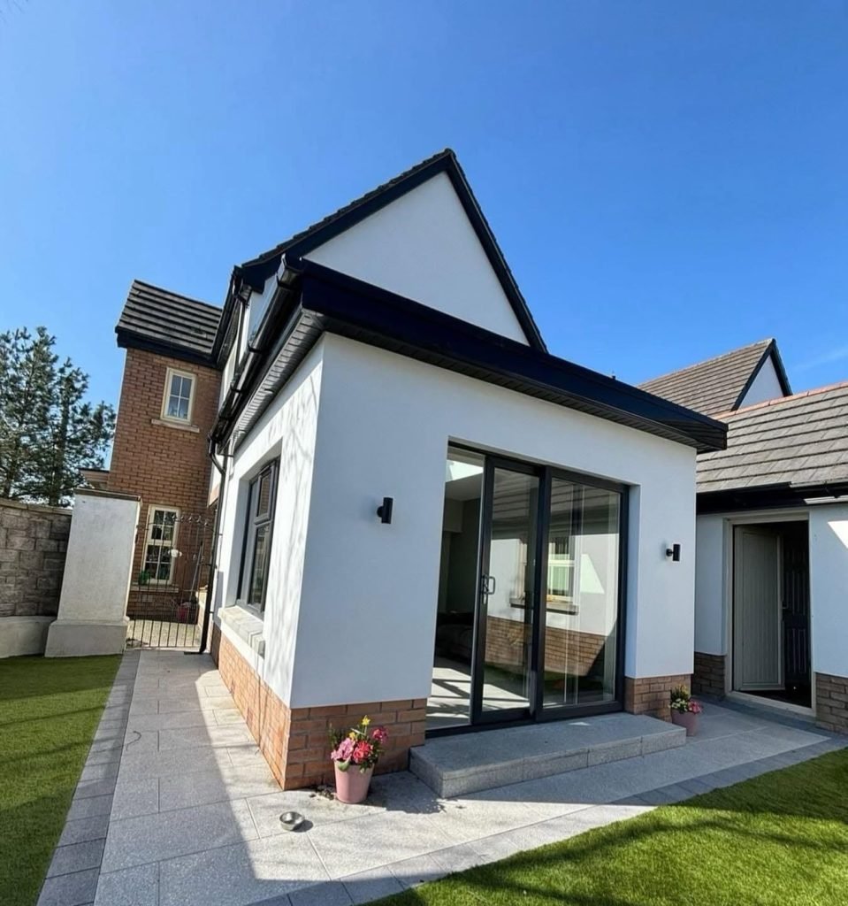 White rendered extension with dark garden doors, brick plinth and a garden lawn