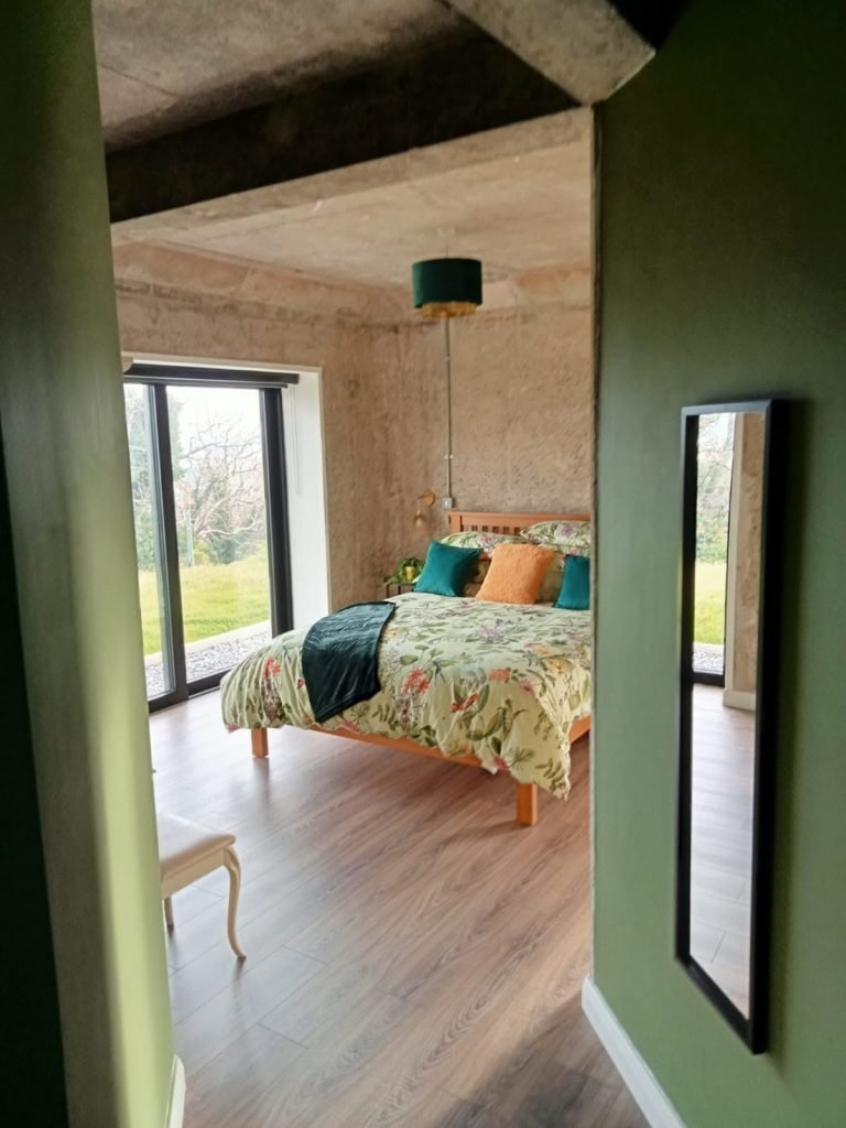 Furnished bedroom with timber flooring, exposed concrete ceiling and glazed garden doors in the Tullybrannigan home